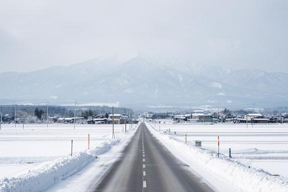 北海道国道12号線の冬景色、雪化粧した田園地帯を貫く直線道路の遠景、両側には白い平野が広がり遠くに山々が望める